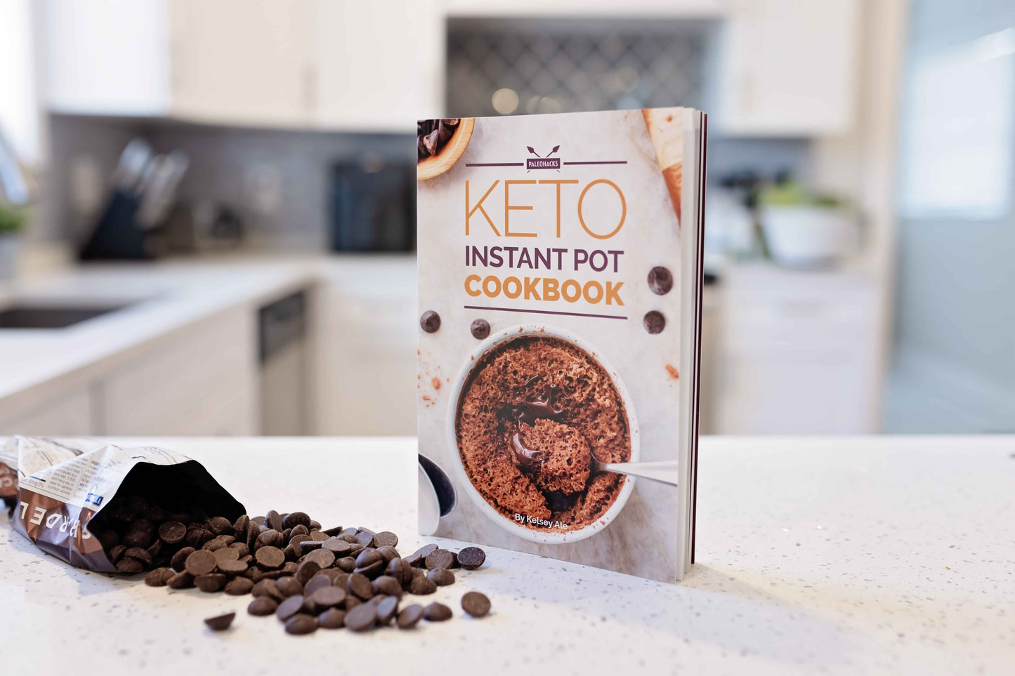 Keto instant pot cookbook stands on a marble kitchen counter top with a pack of chocolate chips spread on the surface.