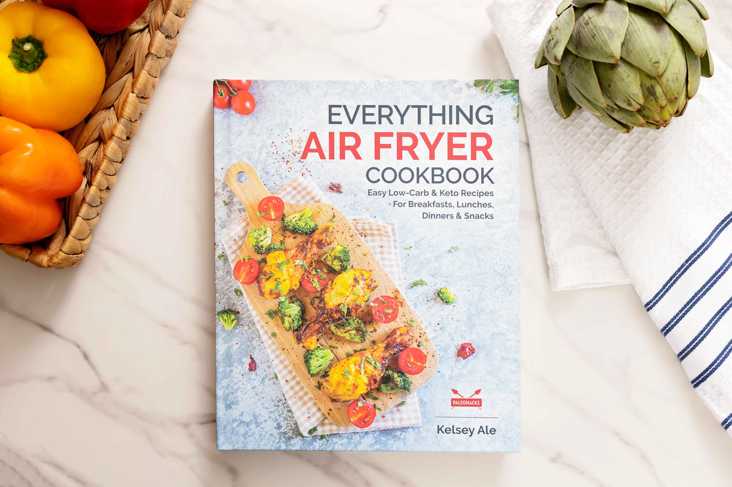 The "Everything Air Fryer" cookbook is laid out on a white marbled surface. Vegetables and a kitchen cloth are visible.