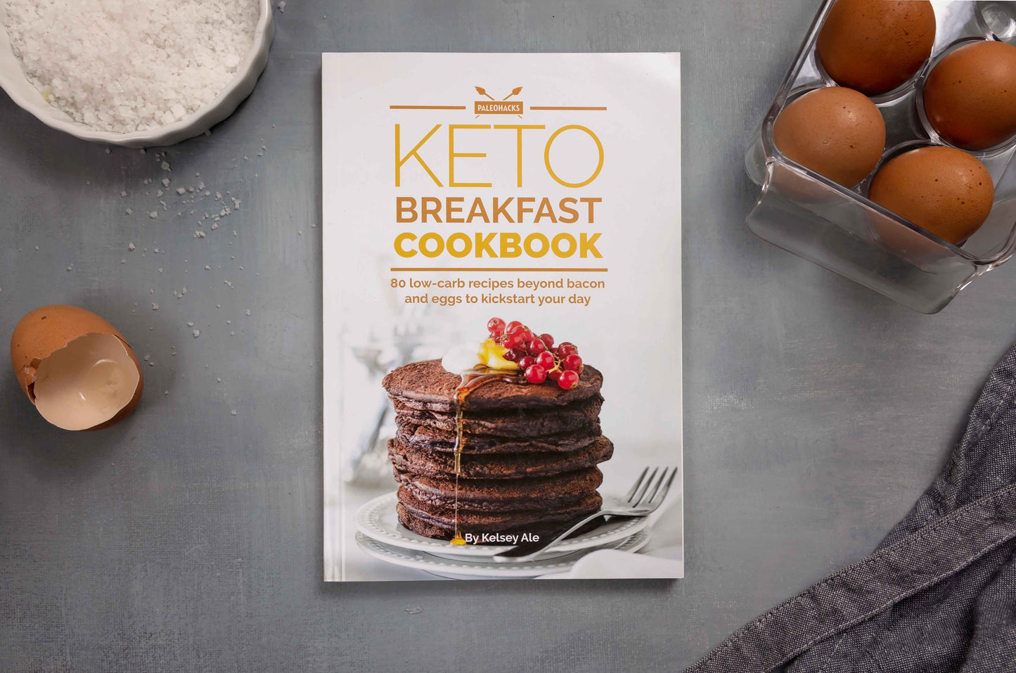 Keto breakfast cookbook placed on a grey surface, surrounded by eggs and sea salt.