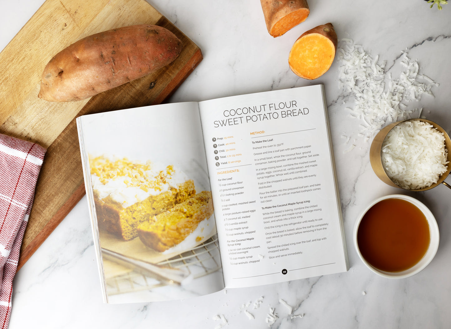 An opened Paleo Snacks Cookbook placed on a cutting board and a marble surface, surrounded by a bowl of honey and shredded coconut.