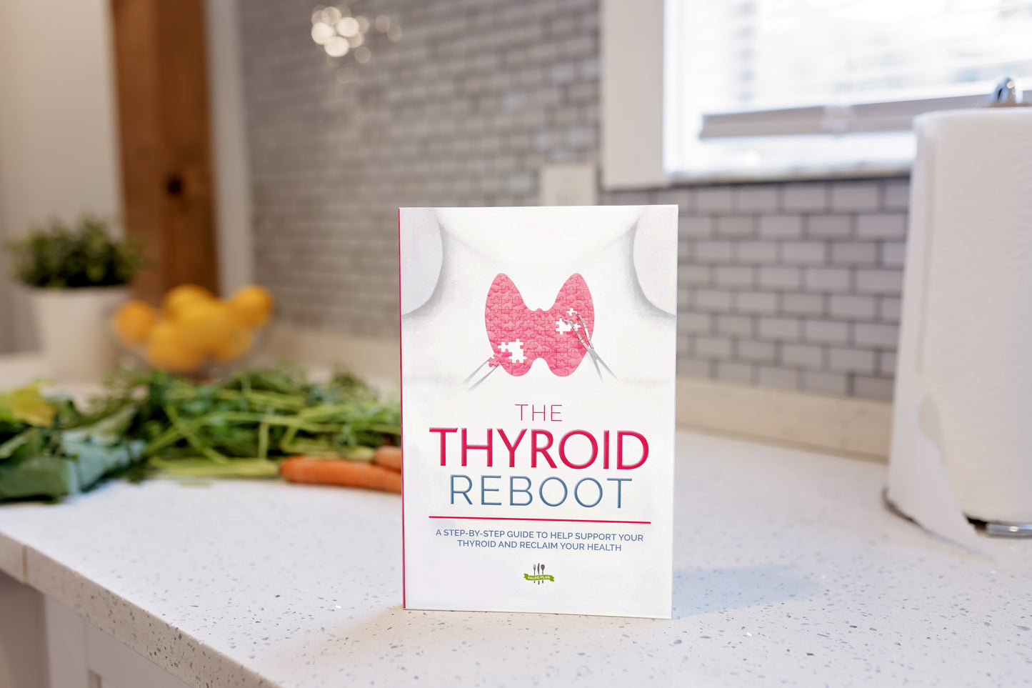 The Thyroid Reboot book stands on a marble kitchen counter. Vegetables and a flower pot can be seen in the background.