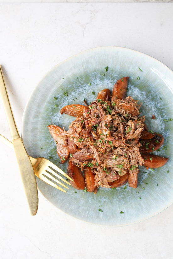 A green plate of spicy peach pork with cutlery placed on a white surface.