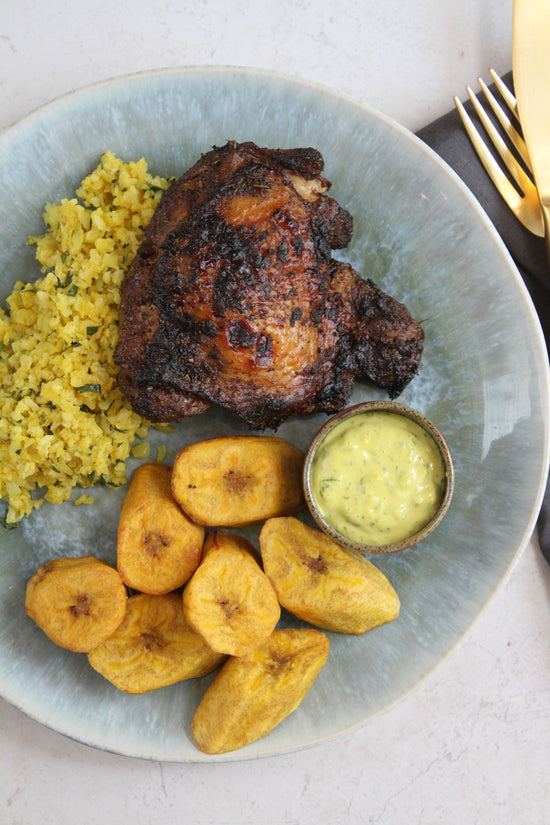 A plate of Jerk chicken meal placed on a marble plain surface.