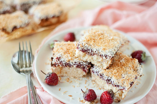 A white plate of coconut strawberry bars on a pink kitchen cloth.