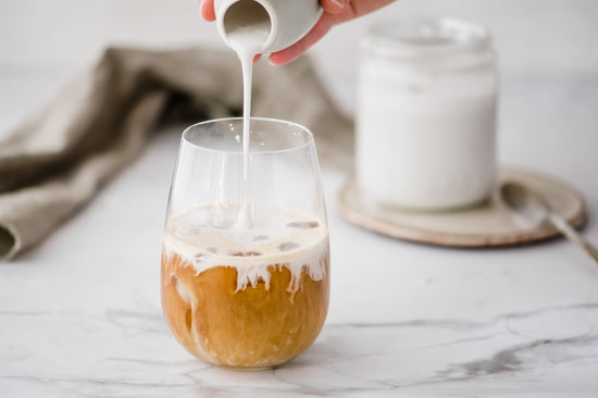 A glass coffee with dairy free French vanilla cream being poured in. A jar of cream can be seen.