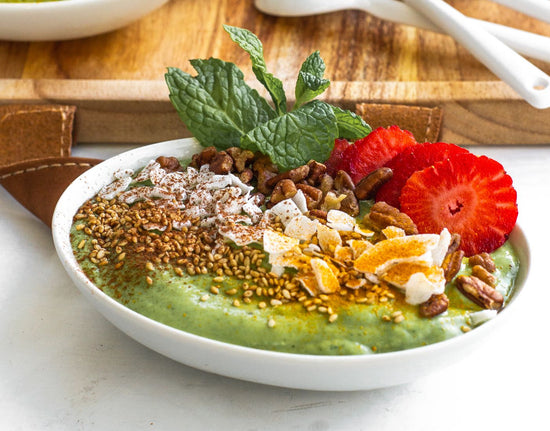 A white bowl of Green Smoothie kept close to a wooden tray on a white plain surface.