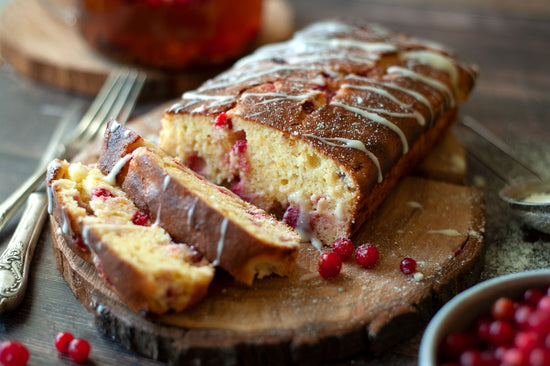 Orange cranberry loaf sliced on a wooden board. A bowl of cranberries is visible.