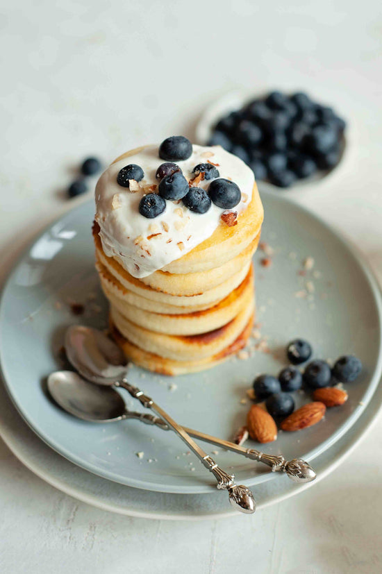 A grey plate of almond pancakes with blueberries and spoons.