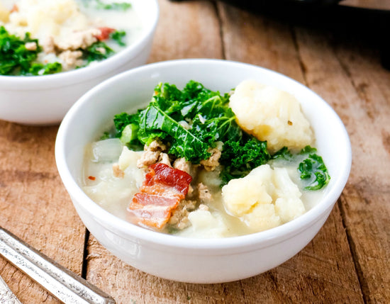 Two white bowl of slow cooker Zuppa Toscana placed on a wooden surface.