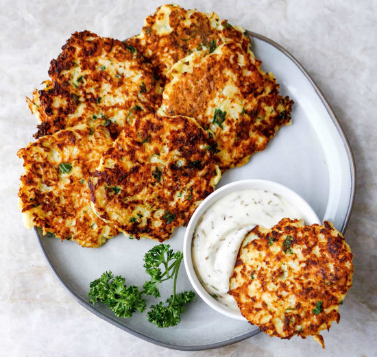 A plate of Cauliflower Hash Browns with a bowl of cream dipping sauce on a marble surface.