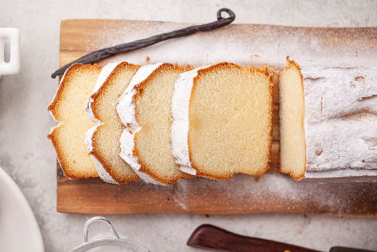 A wooden board of sliced vanilla pound cakes dusted with powdered sugar