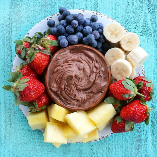 A plate of velvety chocolate and fruits placed on a blue surface.