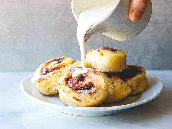 A white plate of cinnamon rolls with someone pouring icing on top.