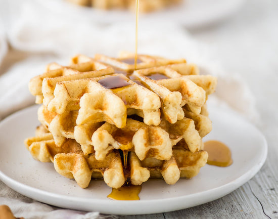 A white plate of churro waffles with syrup drizzled on top