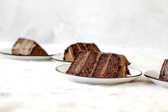 White plates with slices of Classic Chocolate Cake placed on a marble surface.