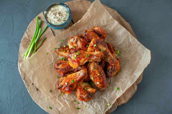 Buffalo Chicken Wings on a brown wrap are placed on a wooden board with a bowl of sauce and spring onions.