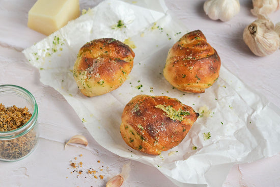 Keto garlic knots on a white paper laid on a marble surface with a jar of garlic and cheese seen.