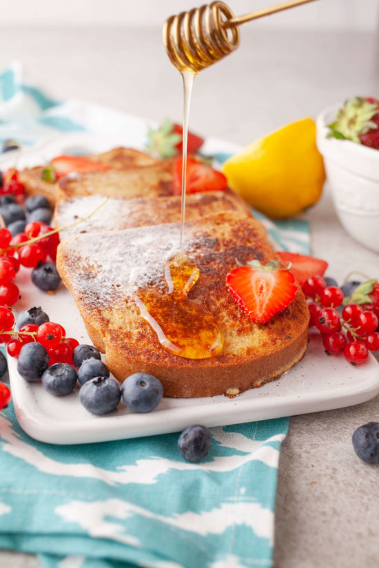 A white tray of French toast with honey drizzle, strawberries and blueberries