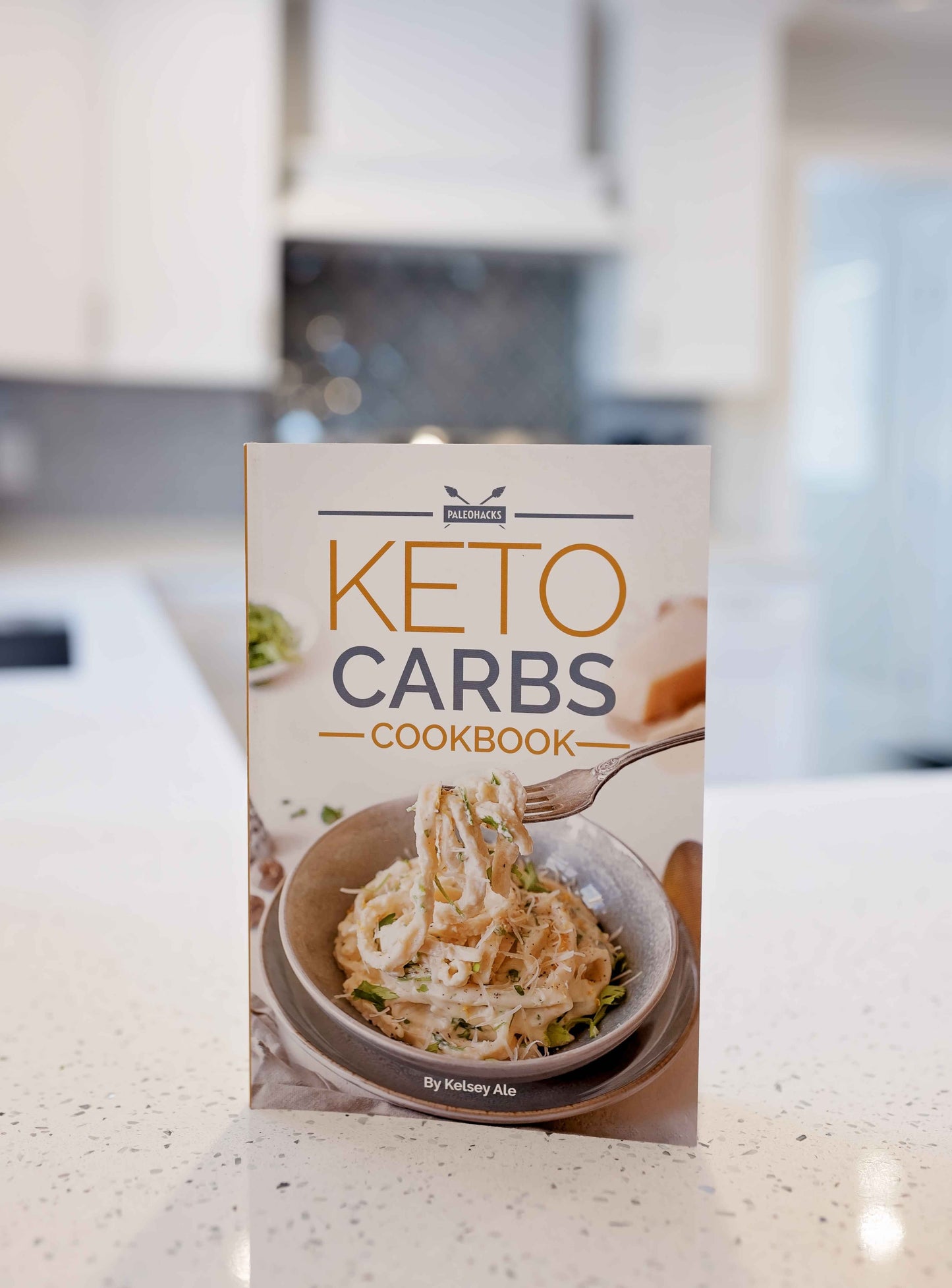 Keto carbs cookbook stands on a marble plain surface.