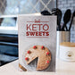 The Keto Sweets Cookbook stands on a kitchen counter. A jar of utensils can be seen.
