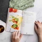 An opened Keto breakfast cookbook laid on a marble surface. Kitchen cloth and utensils can be seen.