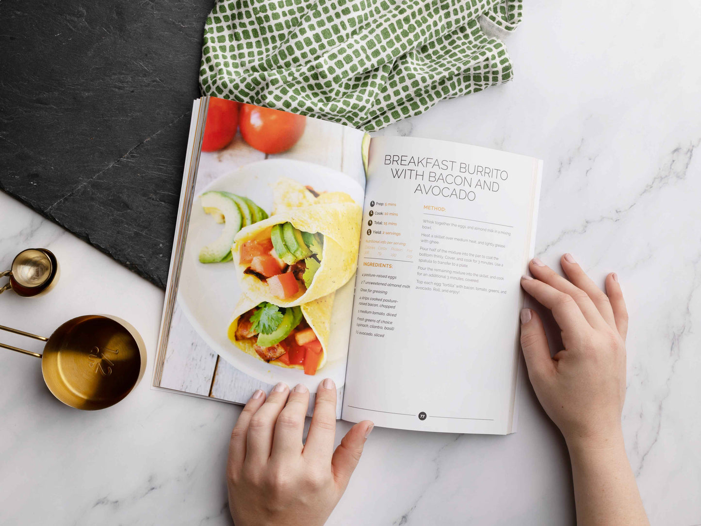 An opened Keto breakfast cookbook laid on a marble surface. Kitchen cloth and utensils can be seen.