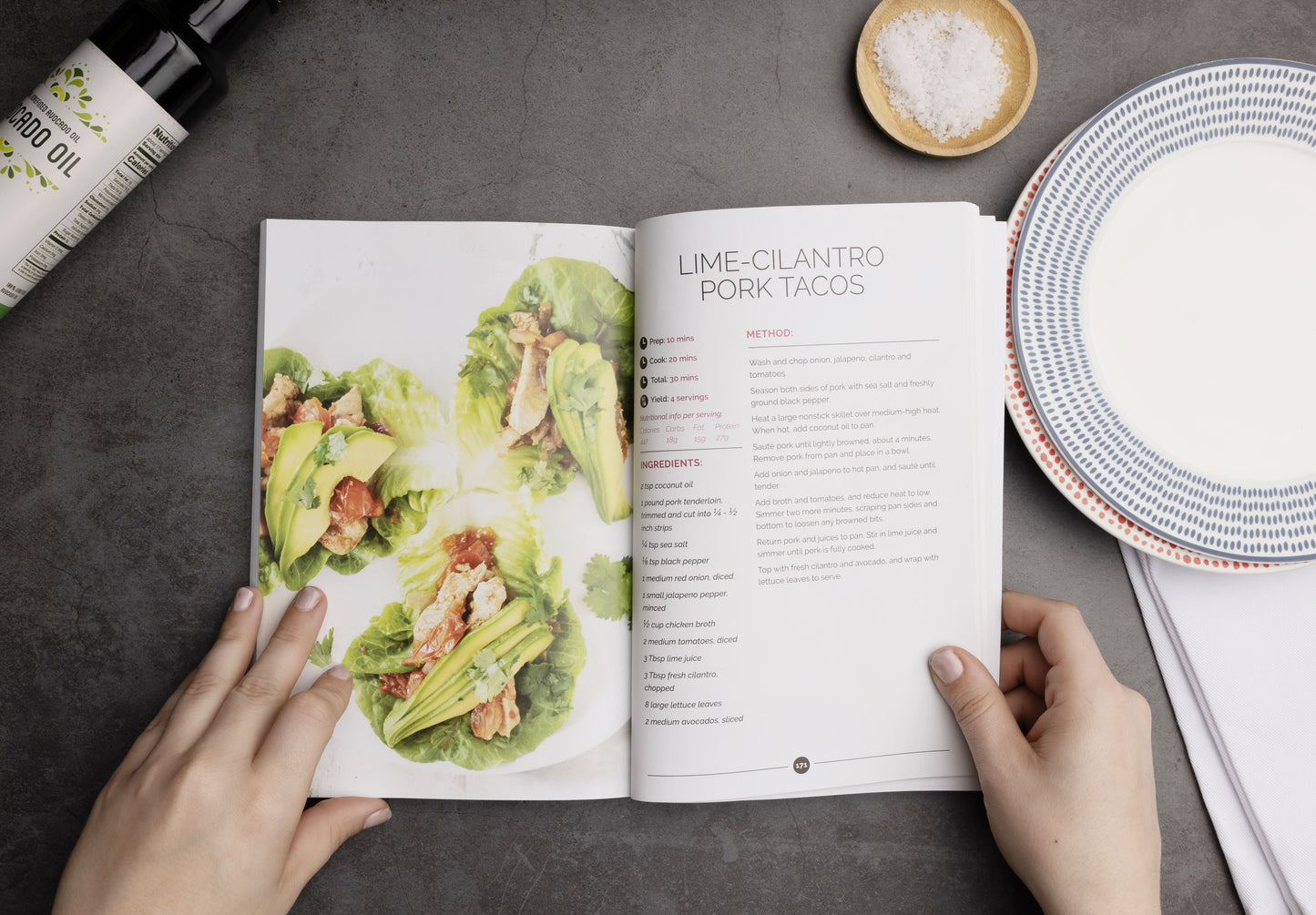 An opened Thyroid Reboot book laid on a plain grey surface. Avocado oil, salt, and a plate can be seen.