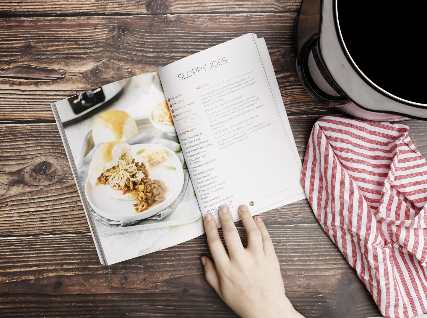 An opened Keto slow cookbook laid on a wooden surface. Cooking utensil and a kitchen cloth can be seen.