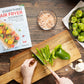 The "Everything Air Fryer" cookbook is placed on a wooden plain surface with a wooden board having sliced vegetables, while a separate bowl of vegetables can be seen.