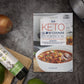 The Keto Slow Cookbook is laid on a plain grey surface. Avocado oil and vegetables can be seen on a wooden board.