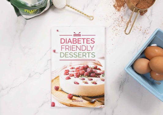 Diabetes Desserts Cookbook sits on a kitchen counter with a bowl of eggs, sweetener and cacao next to it