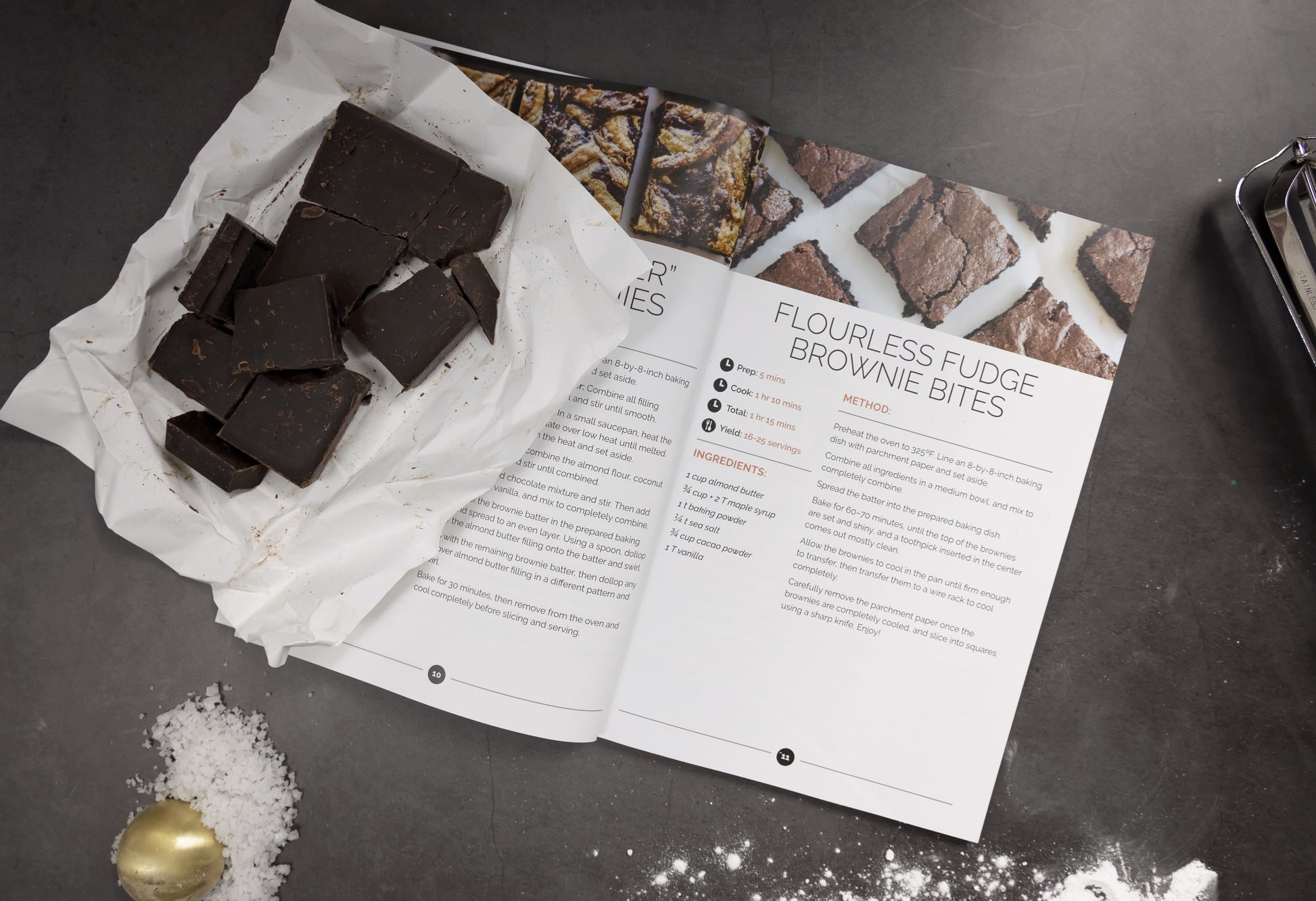 An open Paleo Sweets Cookbook with chocolate bars placed on a white paper on the left-hand pages. A measuring spoon is also visible on the left side.