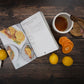 An opened Paleo Slow Cooker Cookbook laid on a wooden surface with citrus fruits and a jar of honey.