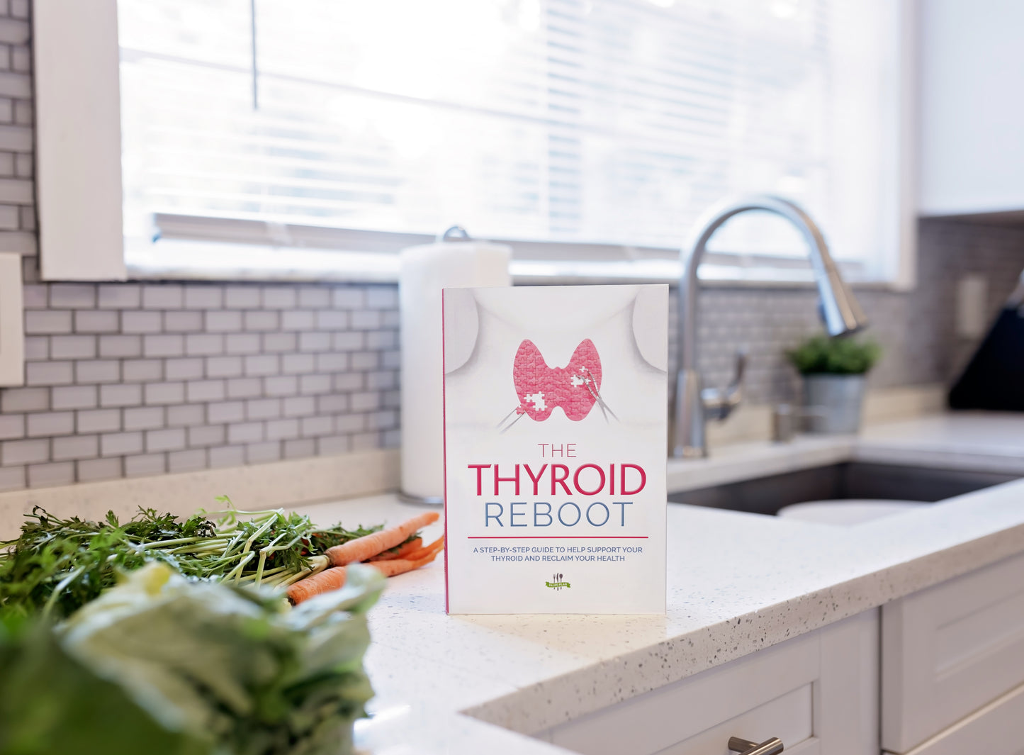 The Thyroid Reboot book stands on a kitchen counter. Vegetables can be seen in the background.