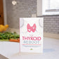 The Thyroid Reboot book stands on a marble kitchen counter. Vegetables and a flower pot can be seen in the background.