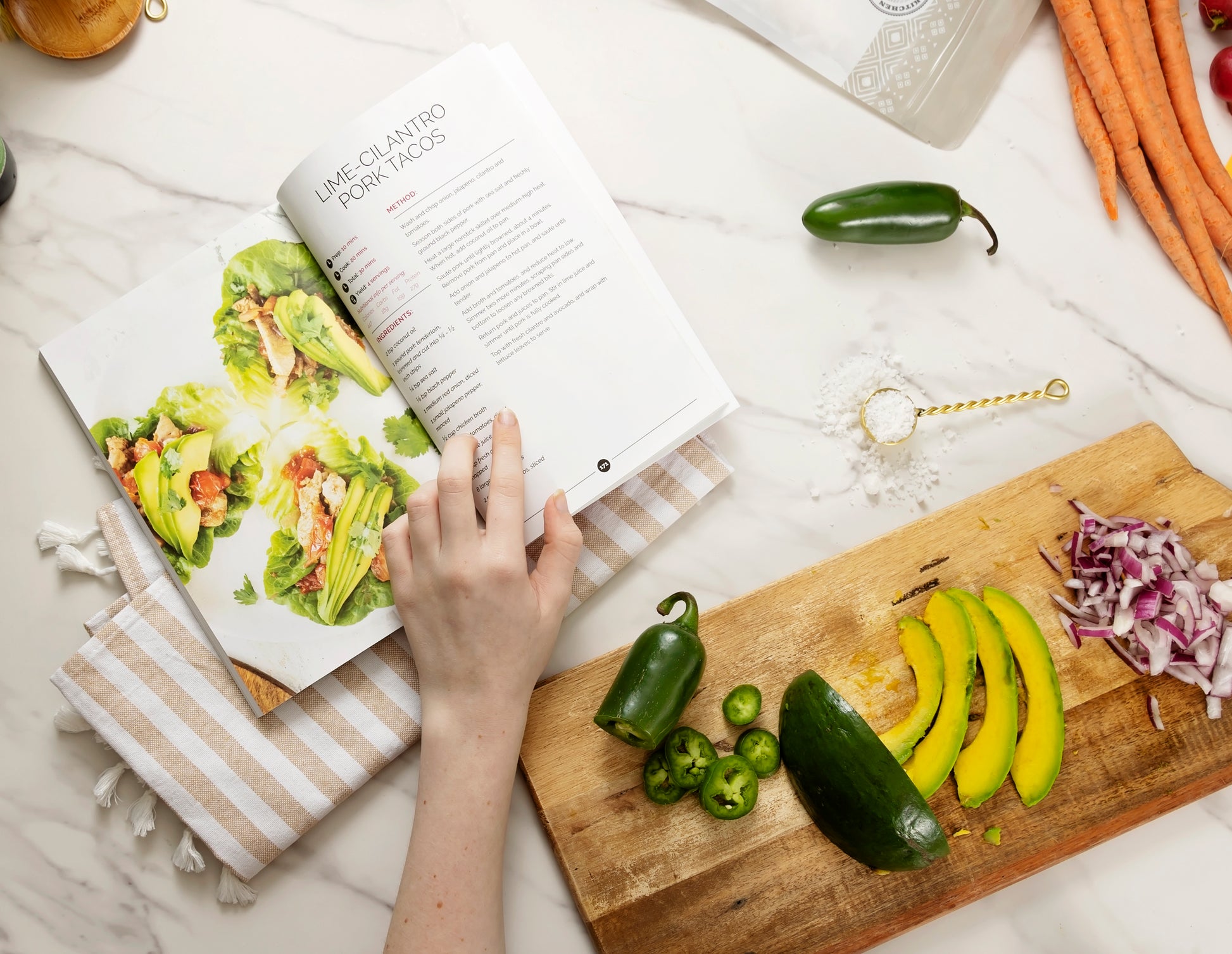 An opened Thyroid Rebook book on a kitchen cloth placed on a marble surface next to a wooden board with sliced vegetables. Measuring spoon, and some vegetables and also be seen.